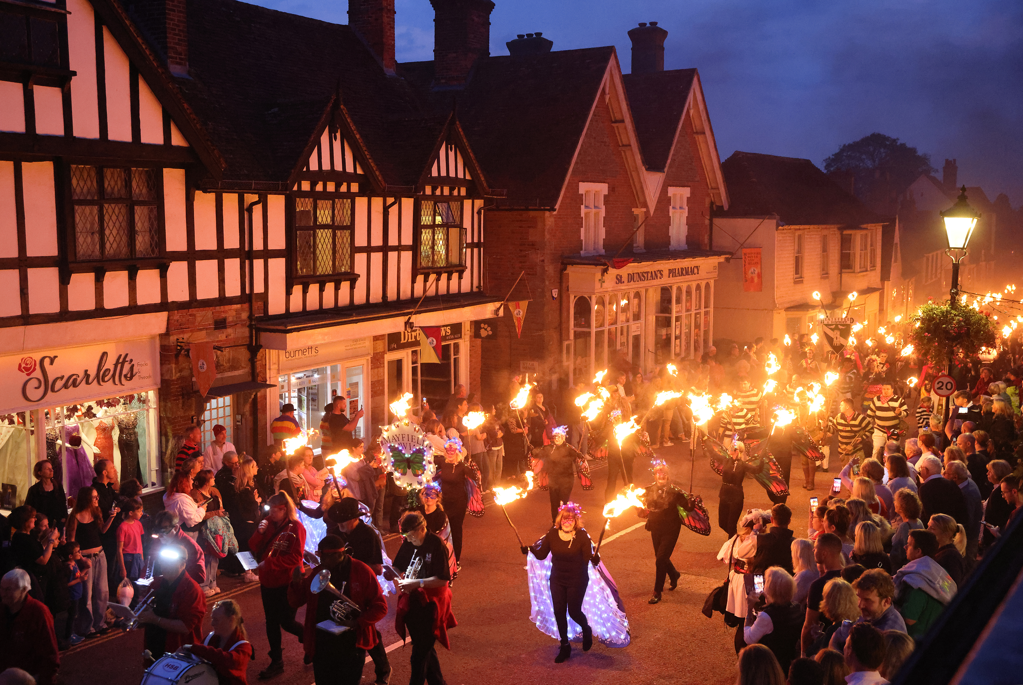 Torchlit procession through Mayfield High Street during the annual Mayfield Bonfire celebrations, with performers, illuminated costumes and crowds lining the historic village streets at dusk.